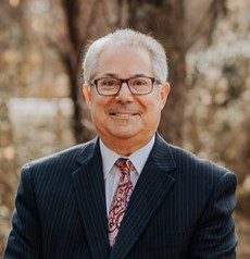 Man in suit with glasses, outdoor background.